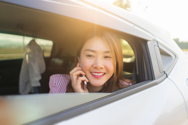 一名亚洲妇女坐在车里打电话、发短信、看手机，司机在一辆概念车里安全地用智能手机说话图片下载
