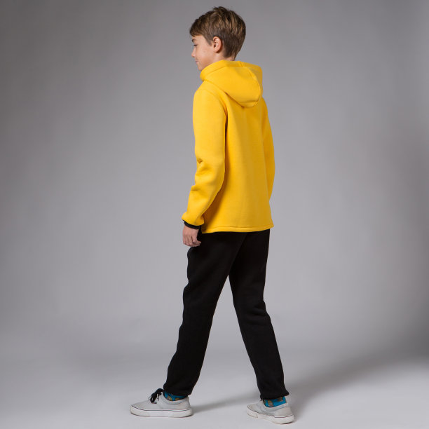 一个穿着黄色卫衣和黑色裤子的少年，工作室拍摄的衣服，在灰色背景上图片下载