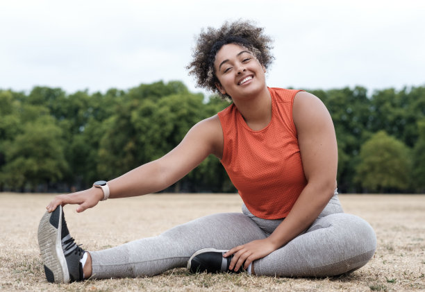 画像微笑的年轻曲线女人伸展在草地上，看着相机。图片下载
