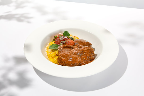 传统的意大利菜-烩牛膝配米兰烩饭。白盘炖骨肉配米饭。夏天意大利餐厅。意大利烩牛肉配上硬皮装饰图片下载