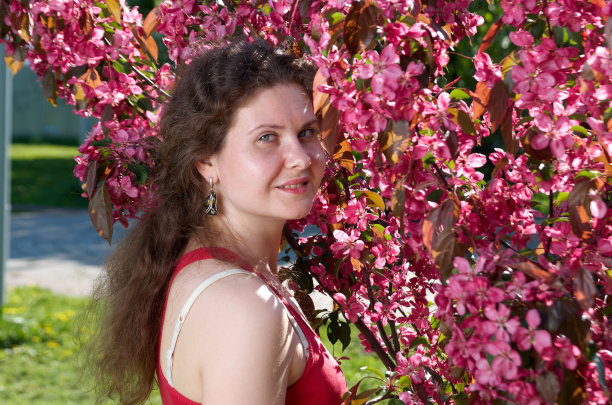 在一个阳光明媚的日子里，美丽的年轻女子的肖像在苹果树盛开的公园里。春天图片下载