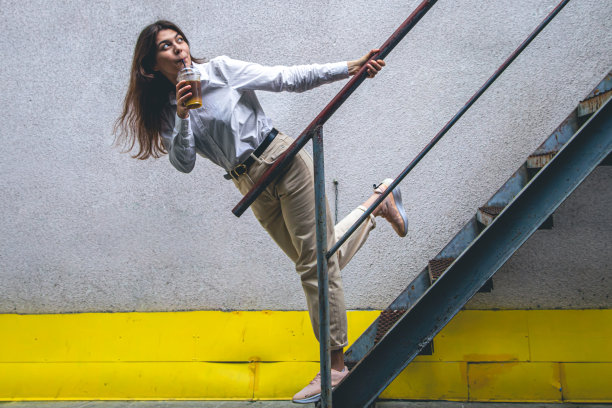 年轻的商务女士在楼梯旁边端着一杯咖啡。图片下载