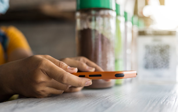 近距离在一个女卖家的双手拿着一个橙色的手机，等待从顾客的扫描。图片下载