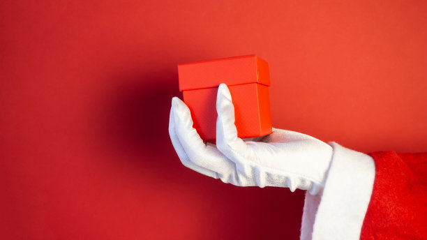 圣诞老人手拿圣诞礼品盒。红色的背景。图片下载