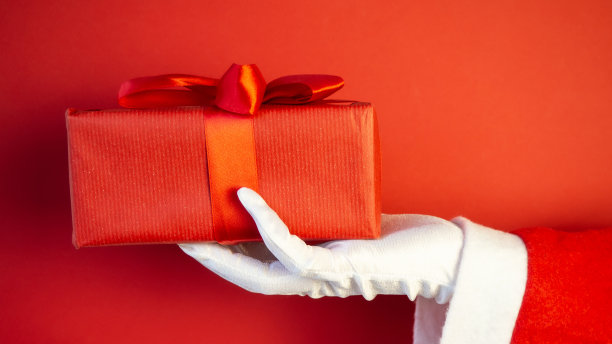 圣诞老人手拿圣诞礼品盒。红色的背景。图片下载
