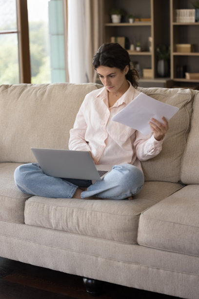 严肃的女人坐在沙发上拿着文件在电脑上工作图片下载
