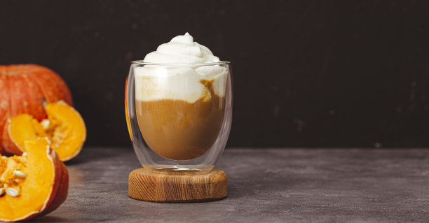 一杯秋季南瓜拿铁，加鲜奶油和香料。咖啡与南瓜和肉桂在黑暗的背景网页横幅图片下载