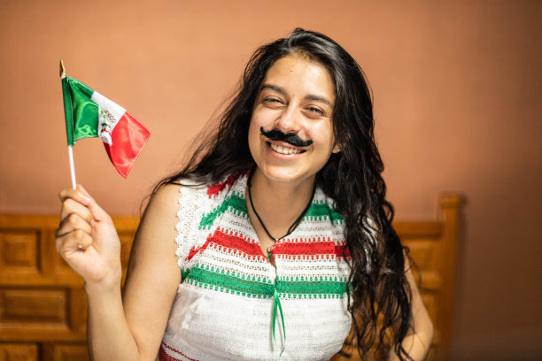 一名墨西哥妇女，穿着代表墨西哥民族色彩的衣服，戴着假胡子，一手拿着墨西哥国旗图片下载