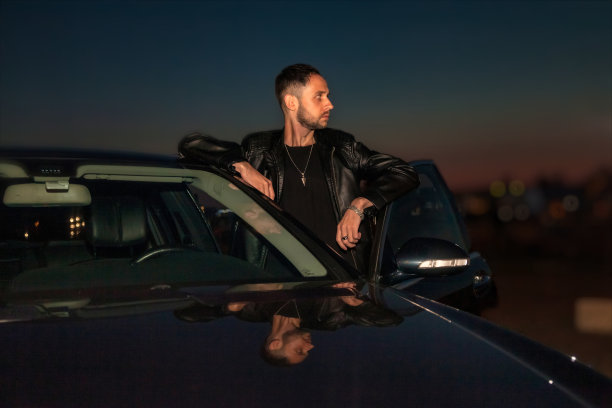 晚上，年轻的司机站在车旁，若有所思地望着别处。夜生活新潮的青春氛围概念。悲伤抑郁的人独自思考问题，感到孤独。复制文本空间图片下载