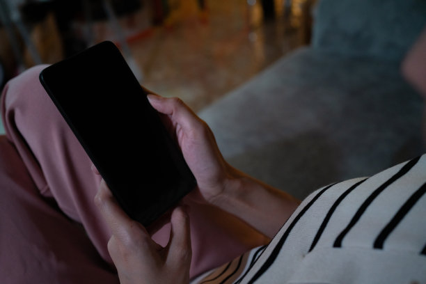 从肩膀上看。晚上在客厅用手机看电视的女人图片下载