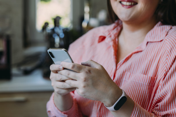 一位面面相觑的快乐的、肥胖的、穿着红衫的女商人，一边在家放松，一边用智能手机发短信图片下载