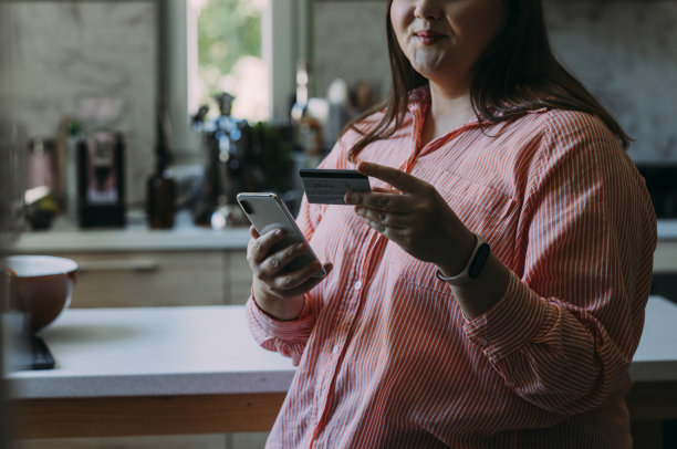 一个无法辨认的快乐的美丽的肥胖女商人在家里放松时用她的信用卡和智能手机转账图片下载