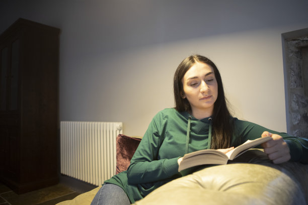 一个年轻的女人在沙发上看书，后面有一个暖气片图片下载