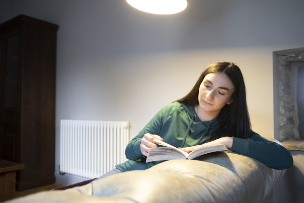 一个年轻的女人在沙发上看书，头顶的灯后面有一个散热器图片下载