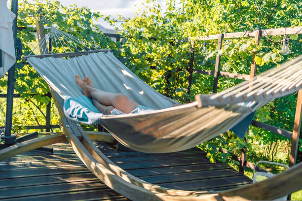 戴着帽子的年轻女子躺在舒适的吊床上，在一个夏天的绿色花园的葡萄木露台上图片下载