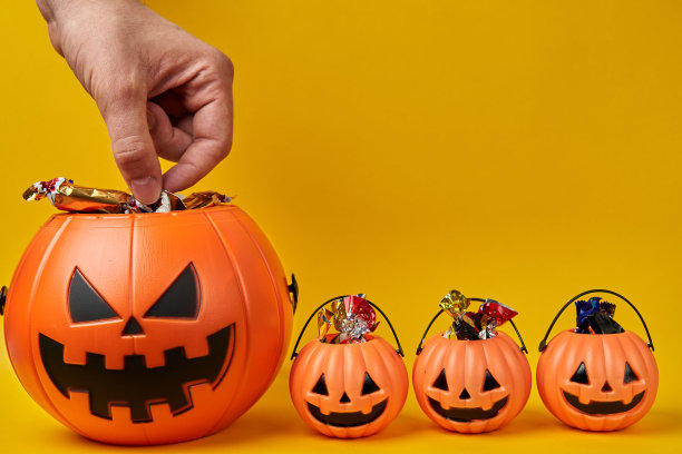 手摘糖果从万圣节大南瓜头篮子小篮子在黄色背景与复制空间图片下载