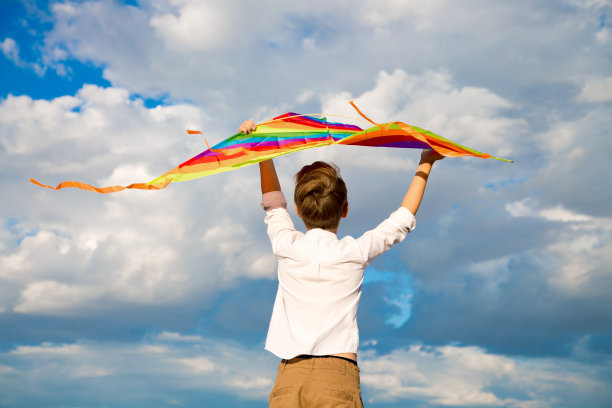 一个穿着白衬衫的英俊男孩，蓝色的天空背景上有一个五颜六色的风筝图片下载