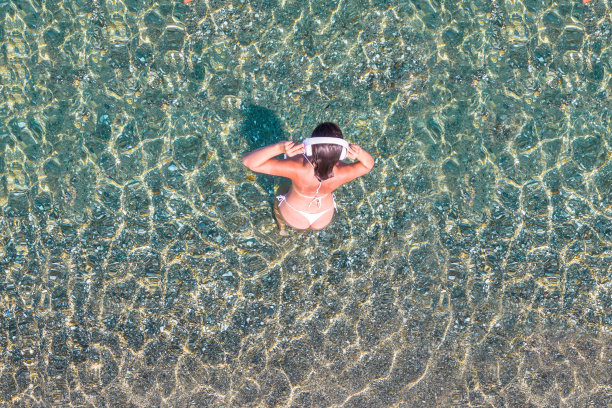 前,鸟瞰图。年轻美丽的女人运动的身体戴着耳机听音乐走在沙滩上的海水比基尼。无人驾驶飞机,直升飞机的照片。暑假。图片下载