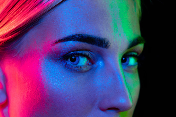 近距离的眼睛美丽的年轻女孩看着相机在粉红色的霓虹灯。概念化妆品、彩妆、自然生态处理、护肤。图片下载