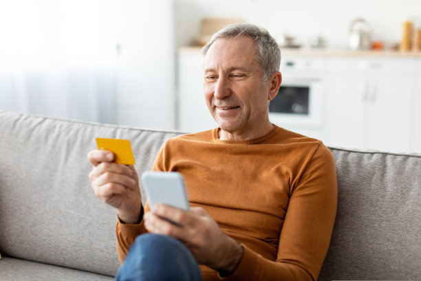 成熟的男人在家里使用电话和信用卡图片下载