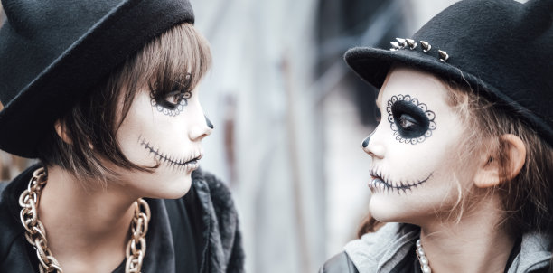 美丽恐怖的小女孩在庆祝万圣节。恐怖的黑白半脸妆，女巫装，时尚形象。恐怖，有趣的孩子在牲口棚在街上的聚会。帽子,夹克图片下载