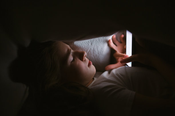 十几岁的小女孩晚上或晚上躺在被窝里看手机。手机成瘾。图片下载