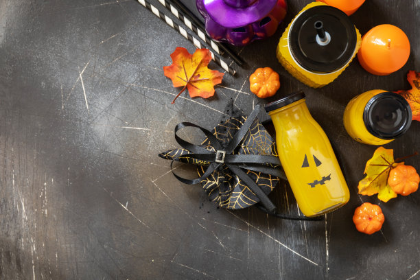 万圣节鸡尾酒等。南瓜鸡尾酒和柠檬水装在玻璃罐里，上面装饰着恐怖的面孔，装饰在深色的石头背景上。从以上观点。副本的空间。图片下载