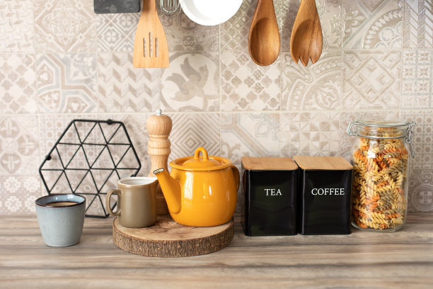 陶瓷罐，黄色水壶，盘子和舒适的装饰在桌子上。厨房里的组织。装咖啡和茶的罐子。厨房用具和木制台面上的用具。时尚的厨房内。图片下载