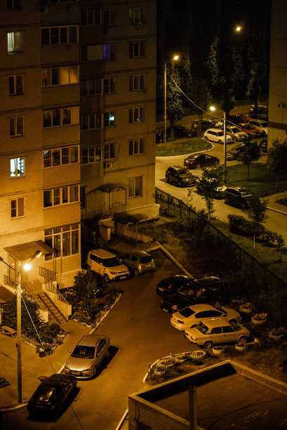 夜间照明下停放在居民楼庭院内的汽车图片下载