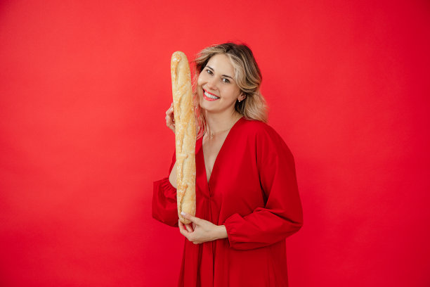 俏皮的微笑的金发女人在红色衣服长法国面包法棍近脸在红色孤立的工作室。做广告图片下载