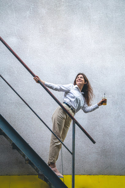 年轻的商务女士在楼梯旁边端着一杯咖啡。图片下载