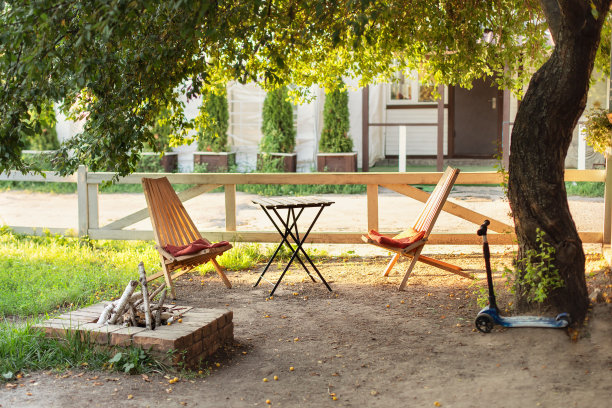 适合野餐或在大自然中休闲的木制户外家具。舒适的室内庭院与桌子和太阳躺椅。夏季花园的椅子和桌子与室外石壁炉。图片下载