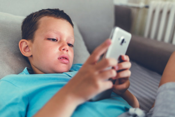 一个小孩在家里用手机看动画片的画像。图片下载