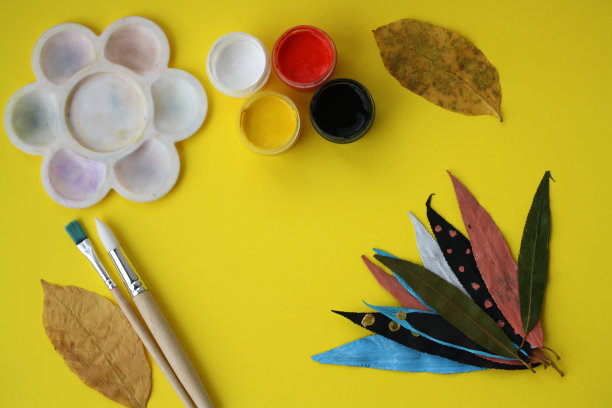 在干燥的秋叶上手绘颜料。孩子们的艺术项目。黄色背景上画的树叶。图片下载