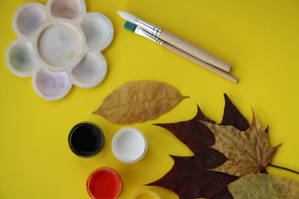 在干燥的秋叶上手绘颜料。孩子们的艺术项目。在黄色背景上晾干树叶、画笔和颜料。图片下载