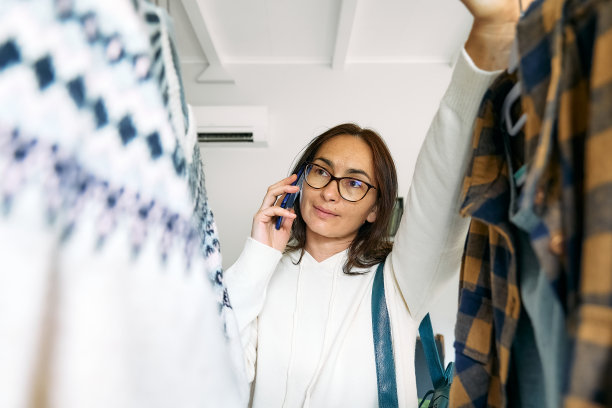 快乐的女人在商店买新衣服。针织毛衣挂在衣架的衣架上。慢时尚。有意识的消费。车库甩卖，再利用衣物，二手和生态消费理念图片下载
