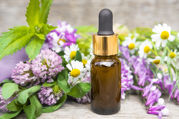 香精油装在棕色玻璃瓶里，背景是木制的野花。洋甘菊，三叶草和草甸草，中草药。图片下载