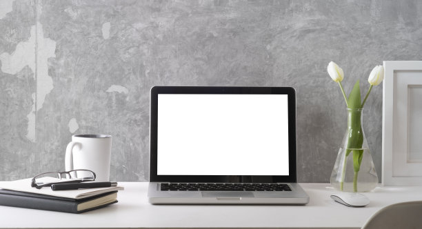 前与笔记本电脑与白色空屏幕，相框，书和咖啡杯在白色的桌子。时尚的工作场所。图片下载