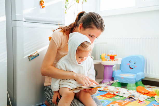 正面看妈妈看书女儿坐在膝盖上用手指展示字母图片孩子微笑感兴趣。图片下载