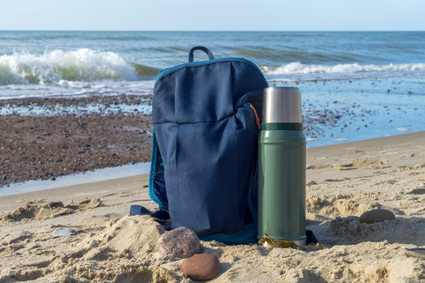 在大自然的背景下，一杯保温瓶茶和一个背包。沿着海边散步。图片下载
