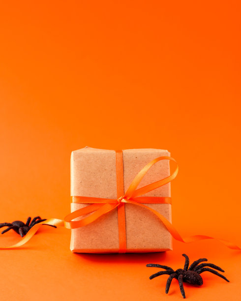 特写棕色礼盒与橙色缎带蝴蝶结和黑色恐怖蜘蛛在橙色模糊的背景与复制空间。秋天节日的概念。图片下载
