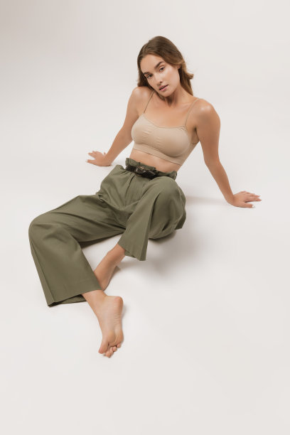 工作室拍摄的漂亮的年轻女孩长卷头发和自然的化妆，穿着露脐上衣和休闲裤子摆姿势在白色背景。图片下载