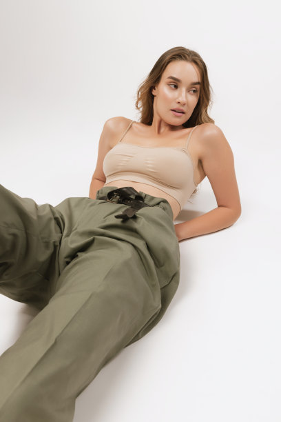 美丽的女人有着长长的卷发，自然的妆容，穿着露脐上衣和休闲裤，在白色背景下摆姿势。图片下载