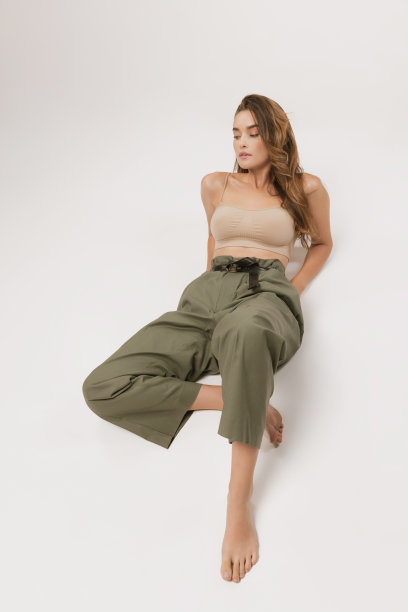 工作室拍摄的漂亮的年轻女孩长卷头发和自然的化妆，穿着露脐上衣和休闲裤子摆姿势在白色背景。图片下载