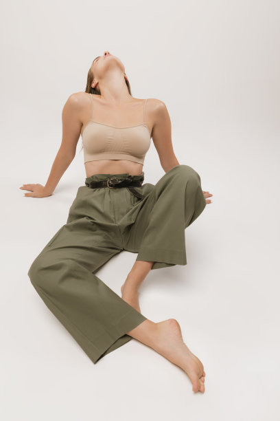 工作室拍摄的漂亮的年轻女孩长卷头发和自然的化妆，穿着露脐上衣和休闲裤子摆姿势在白色背景。图片下载