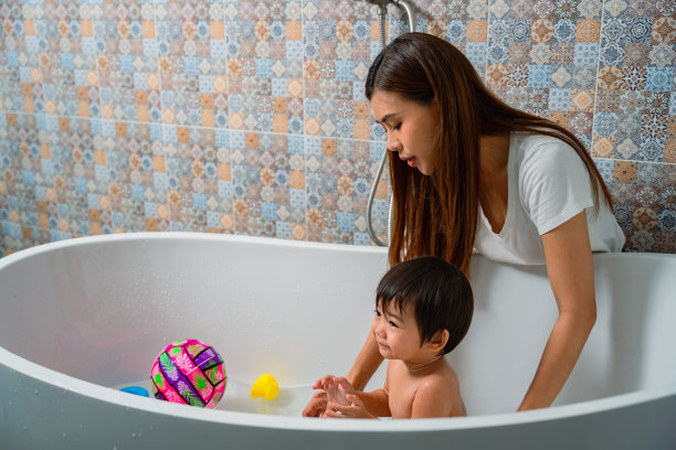 妈妈在浴室的浴缸里给可爱的小儿子洗澡。图片下载