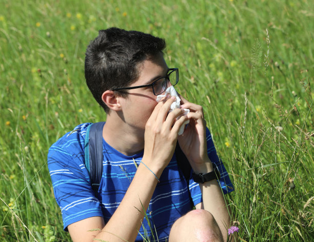戴眼镜的小男孩在草地上因为过敏擤鼻涕图片下载