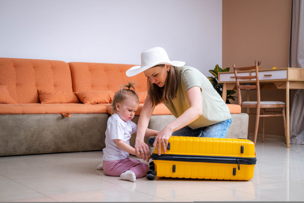 母亲和女婴带着黄色的行李箱行李和衣服，一家人准备在家里度假旅行图片下载