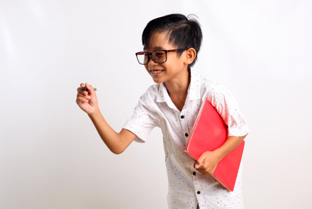 聪明的亚洲男孩站着写东西，拿着一本书。孤立在白色背景中图片下载