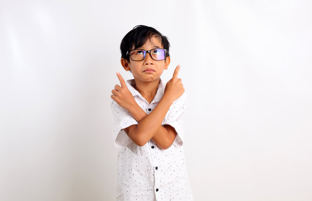 深思熟虑的亚洲男孩站着，用双手指着上面。孤立在白色背景中图片下载